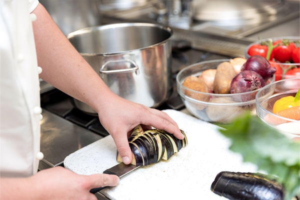 Eine Person vom Küchenpersonal schneidet eine Aubergine. Eine Person vom Küchenpersonal schneidet eine Aubergine.