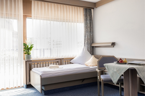 Ein beispielhaftes Patientenzimmer mit großen Fenstern, Bett und Sitzecke.