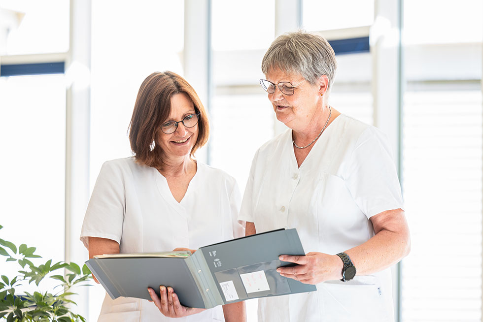 Zwei Mitarbeiterinnen besprechen die Patientenakte. Zwei Mitarbeiterinnen besprechen die Patientenakte.