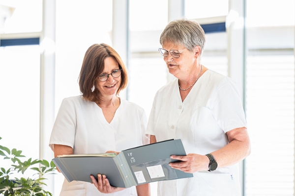 Zwei Mitarbeiterinnen besprechen die Patientenakte. Zwei Mitarbeiterinnen besprechen die Patientenakte.