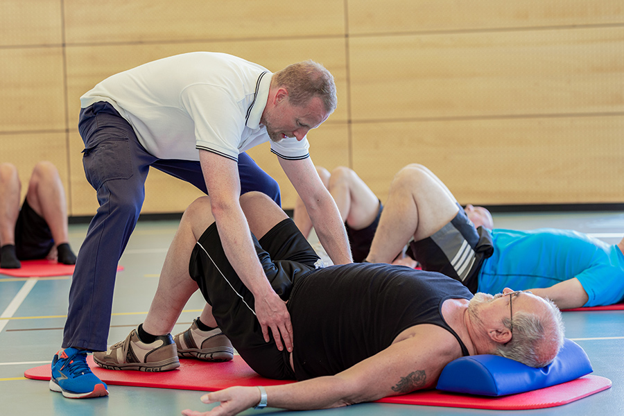 Ein Therapeut leitet Patienten beim Beckenbodentraining auf Gymnastikmatten an.